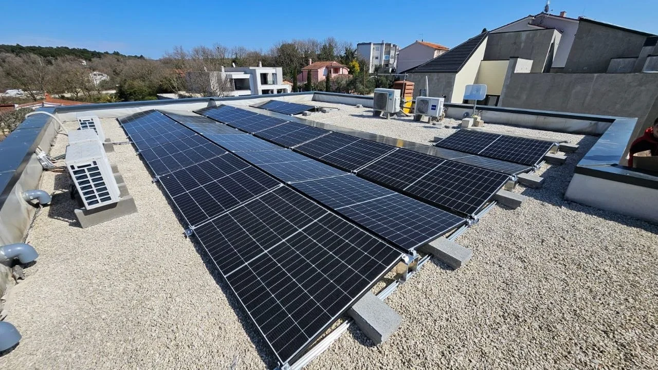 Redovi solarnih panela na ravnom šljunčanom krovu, s kućama u pozadini.